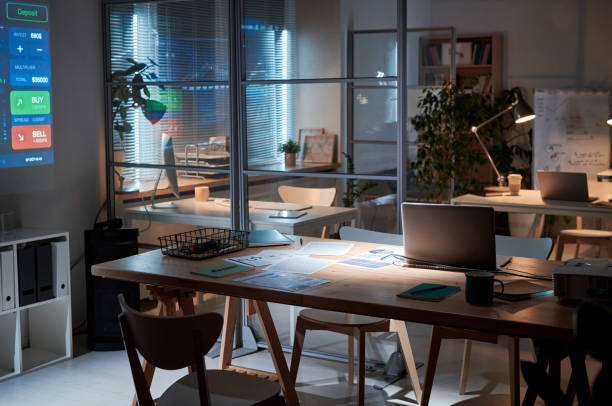 Image of workplace with documents and laptop on it in empty dark board room at office