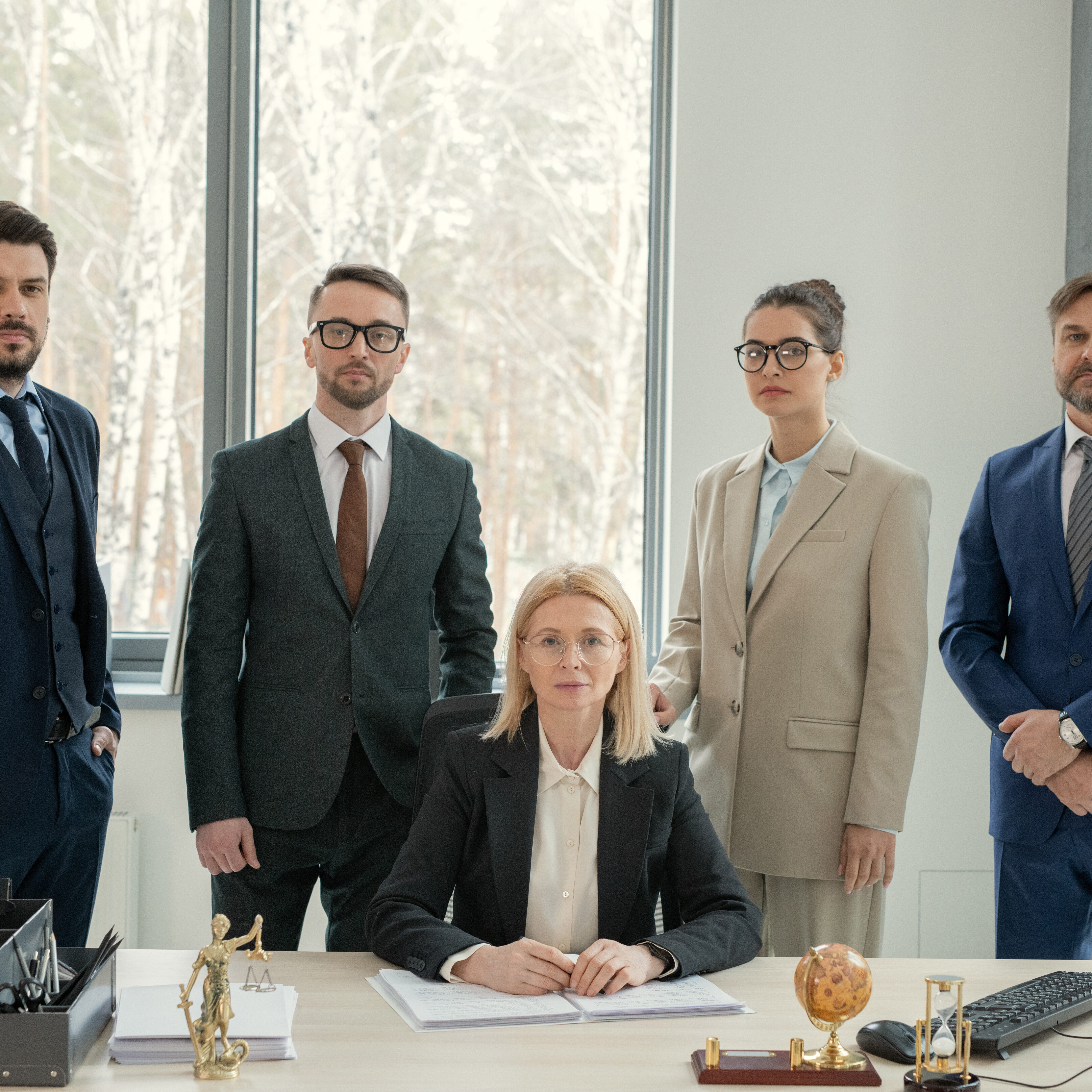 Serious mature female chef of law firm surrounded by lawyers sitting with documents at desk in modern office